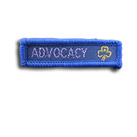 blue rectangle woven badge with the word Advocacy written in lilac in capital letters and a gold trefoil after the writing