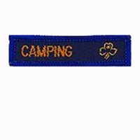 blue rectangle woven badge with the word camping sewn in gold in capital letters and a gold trefoil after the writing
