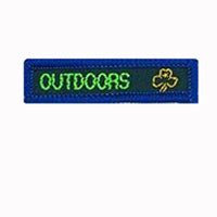blue rectangle woven badge with the word outdoors sewn in lime green in capital letters and a gold trefoil after the writing