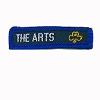 blue rectangle woven badge with the words the arts sewn in white in capital letters and a gold trefoil after the writing