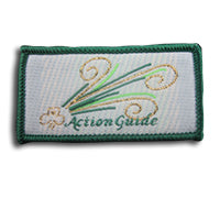 rectangular cloth bound badge with green trim around the edges, trefoil in gold, Action Guide written in green and stripes of green and gold on a white background
