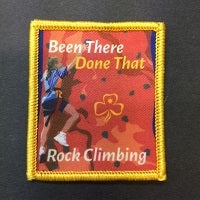 square bound badge that has a picture of a girl in guide uniform rock climbing on an orange coloured climbing wall. The badge is bound in yellow thread.