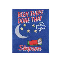 unbound cloth badge that shows a girl in a red sleeping bag sleeping under a quarter moon and some gold stars on a navy blue background