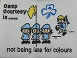Unbound fun badge. Wording - Camp Courtesy is not being late for colours. Embroidered picture of Guides around a flagpole on a white background. 