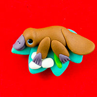 handmade clay brooch with a brown platypus on a green leaf