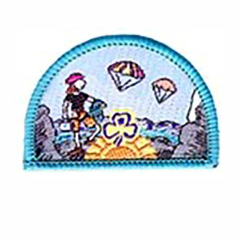 a semi circled shaped badge bound in teal with a picture of a girl hiking with parachutes in the sky