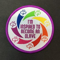 round badge that is bound in purple with I'm inspired to become an olive in the centre with a rainbow of swirls with the trefoil on the ends