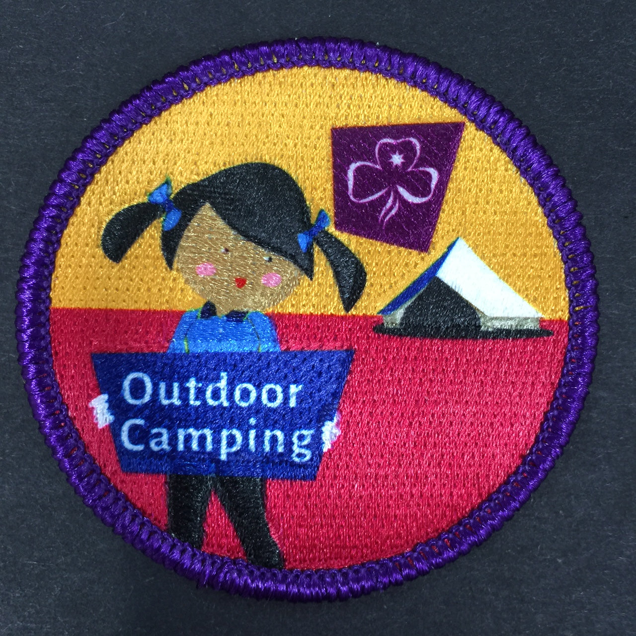 a round badge bound in purple with a guide and a tent 