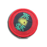 a round badge bound in red with a banksia flower in the middle