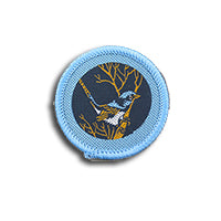 a dark blue round badge bound in light blue with a blue wren on it'