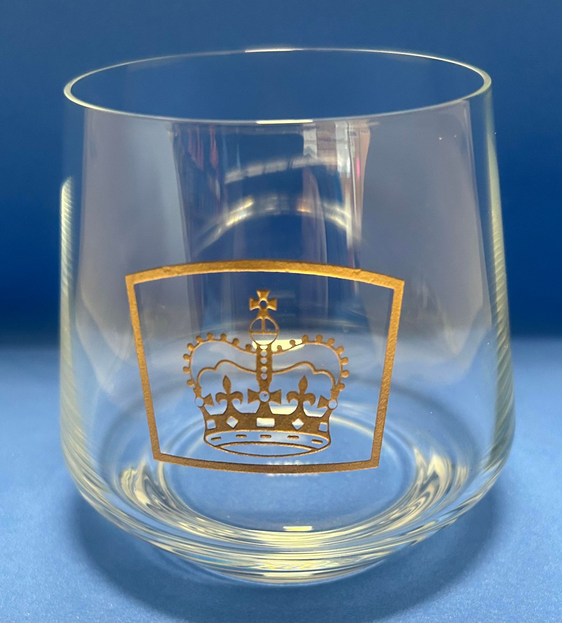 a small glass tumbler with the queens guide logo etched in gold