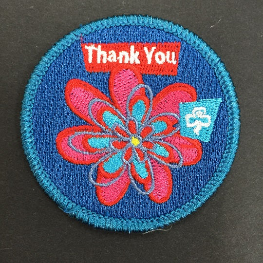 Round bound badge with pink and blue flower on a  blue background.  Thank You in white on a red background