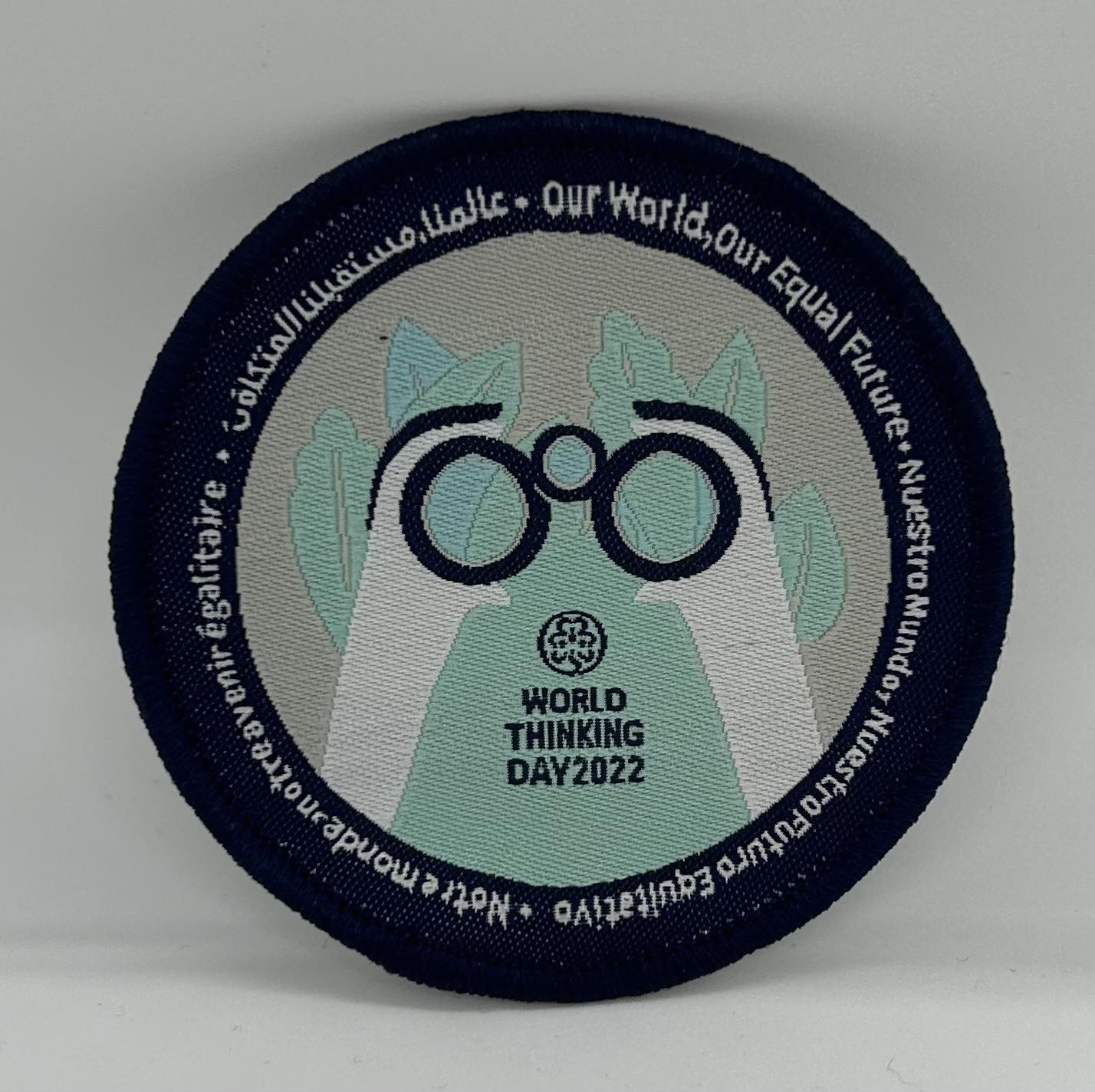 a round badge with binoculars being held by a pair of hands and bound in navy