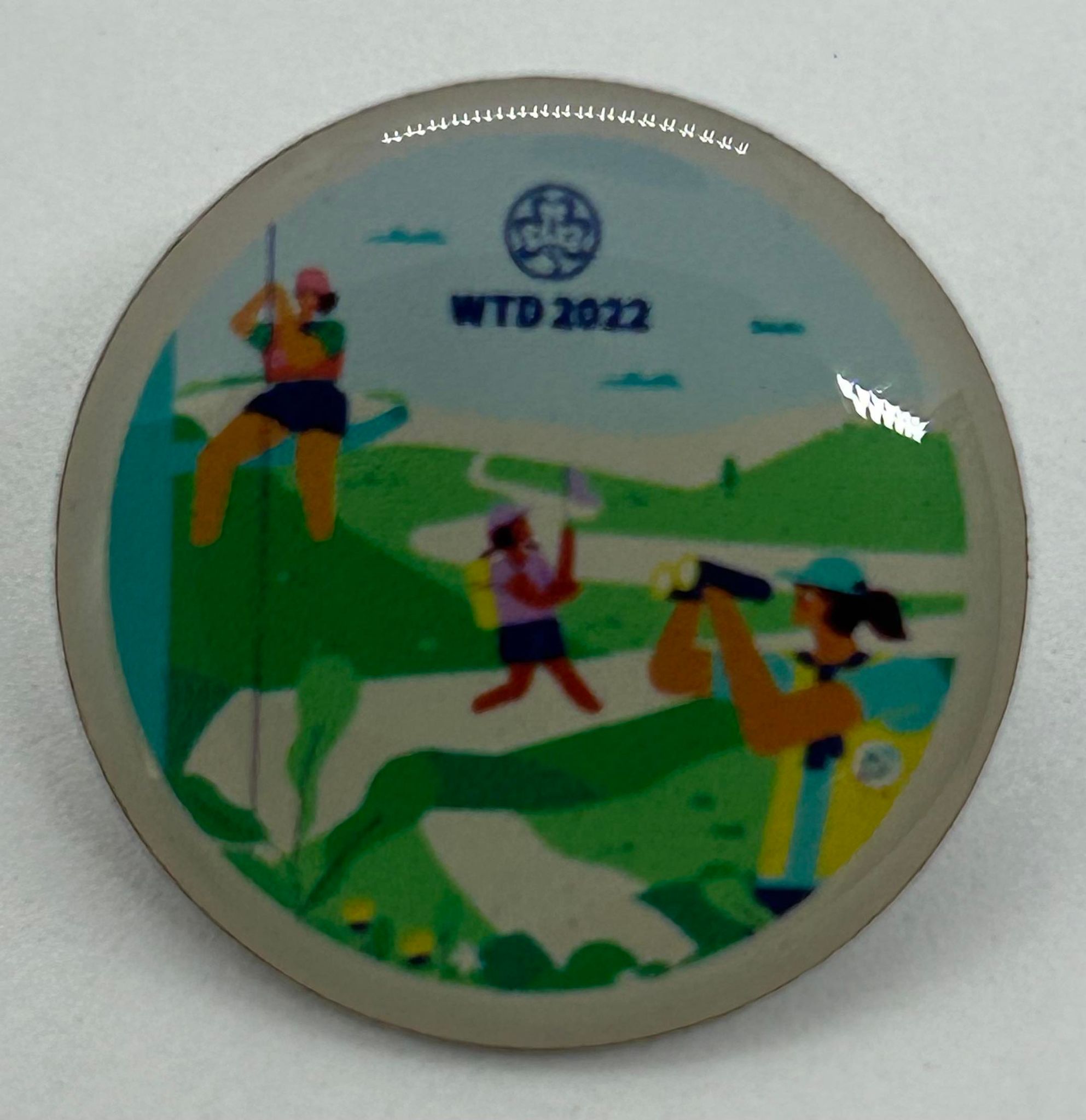 a round metal badge with girls outdoors on it