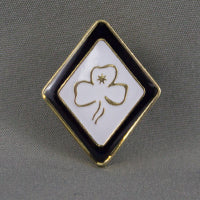 diamond shape metal badge with white enamel front with blue border with a gold trefoil in the centre