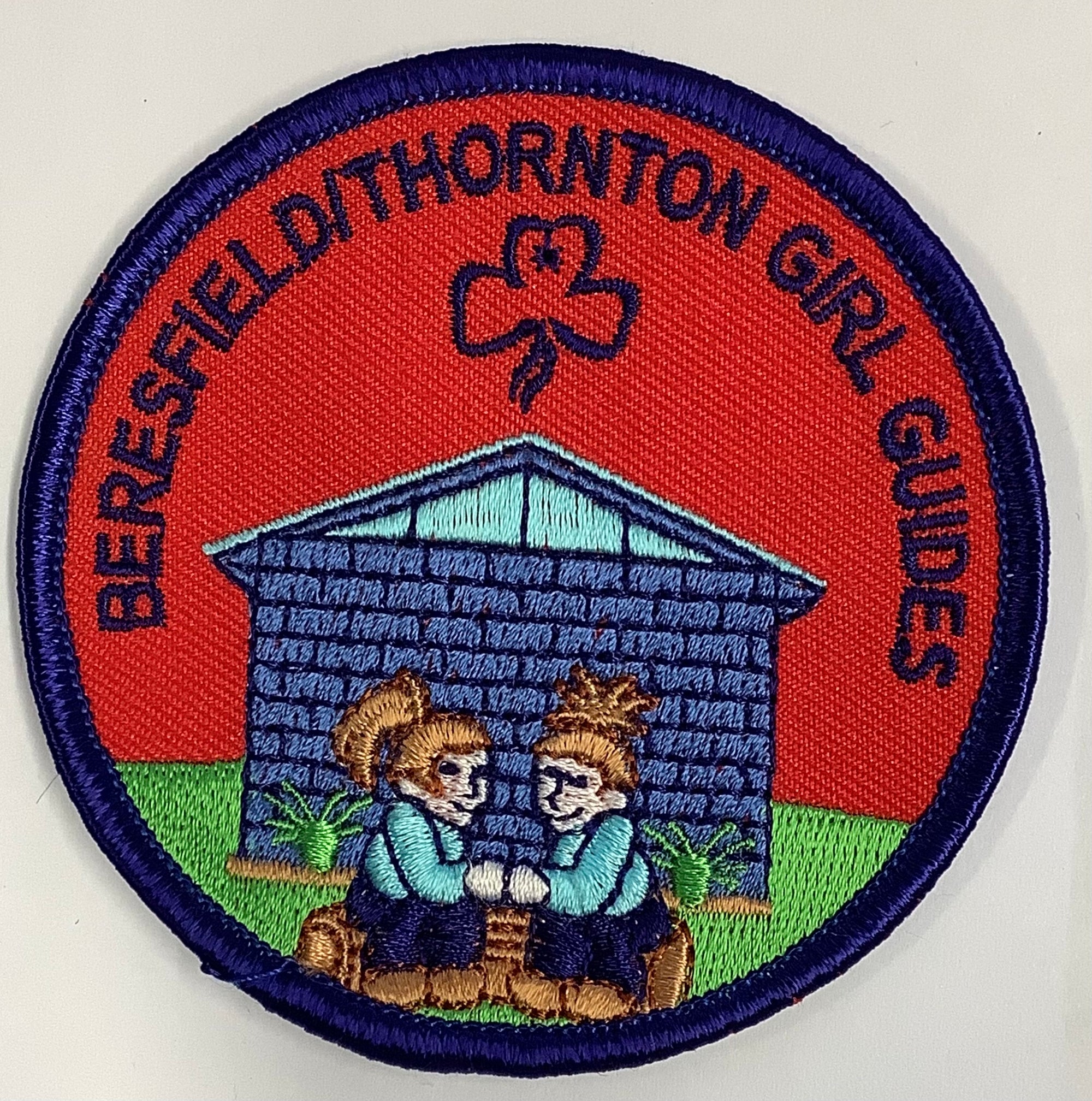 a round bound badge with Beresfield Thornton girl guide hall and two guides on it