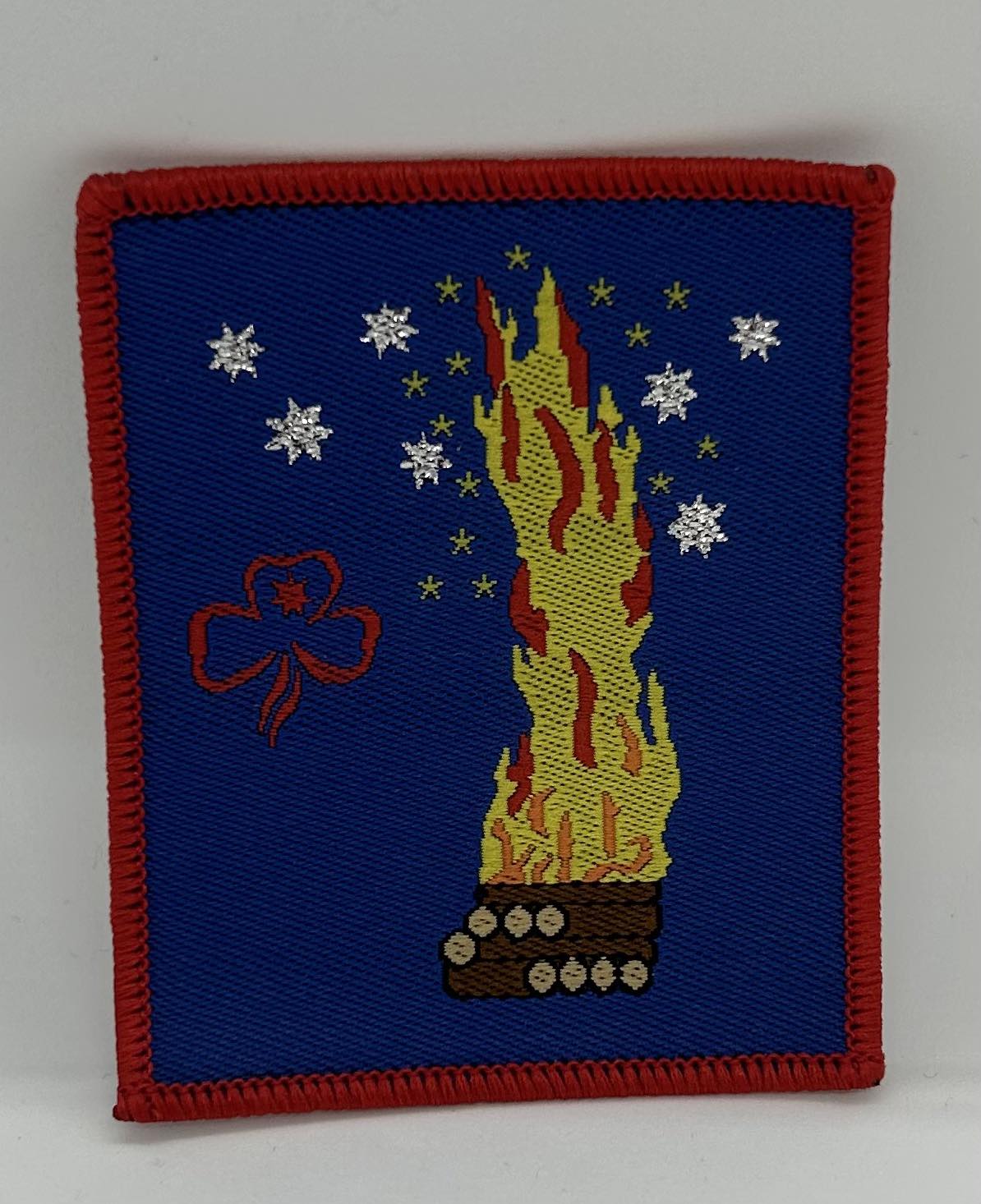 a square blue badge bound in red with a campfire on it