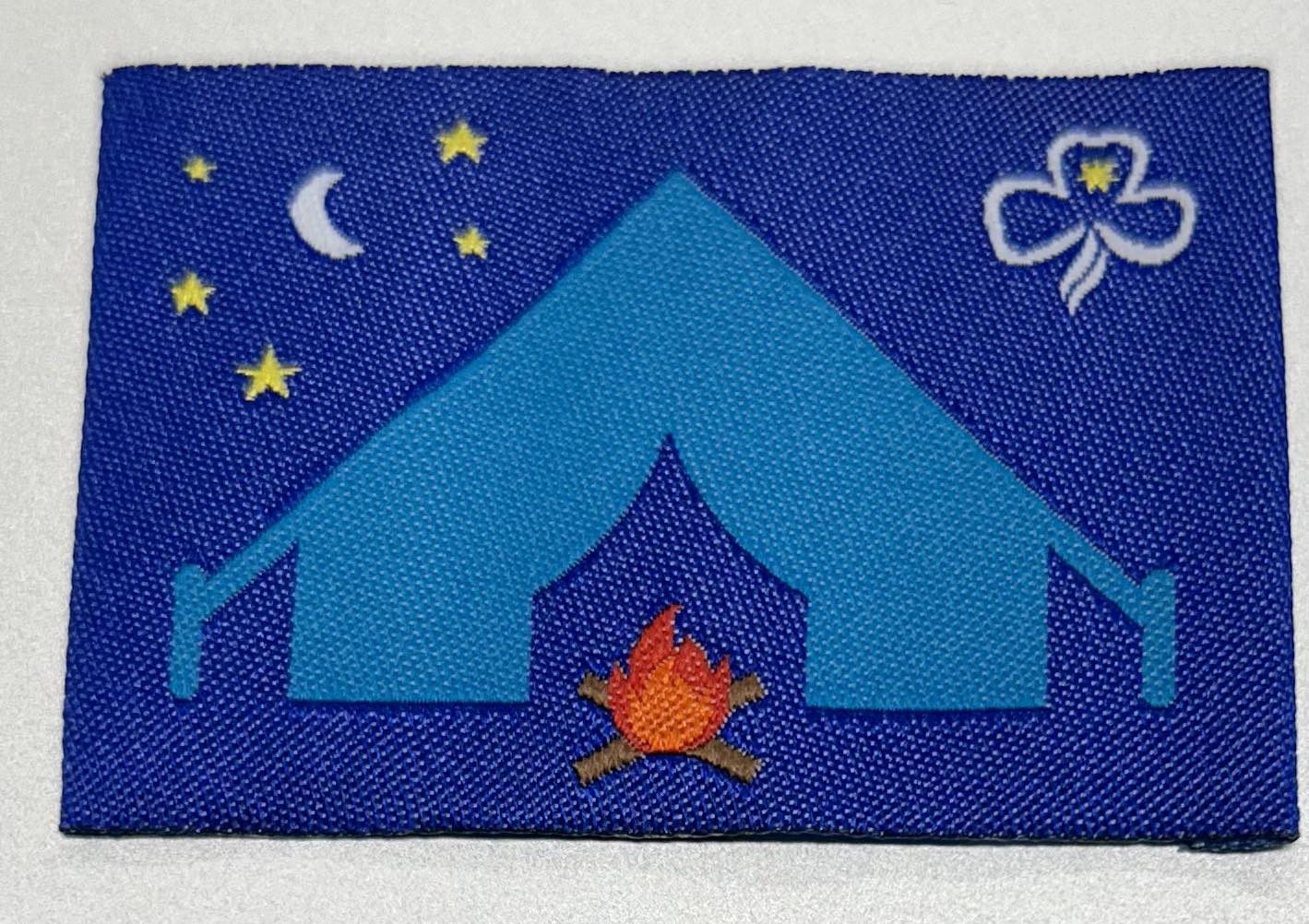 an unbound rectangular badge that has a royal blue background with a light blue tent, campfire, moon and stars