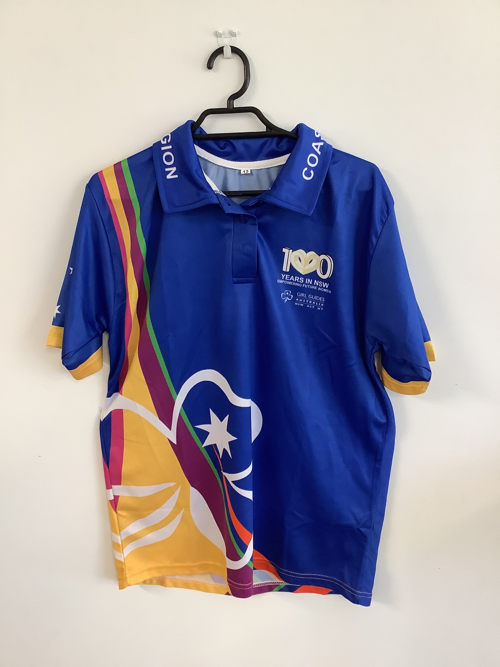 a blue polo shirt with a large white trefoil and coloured swirls down the right side