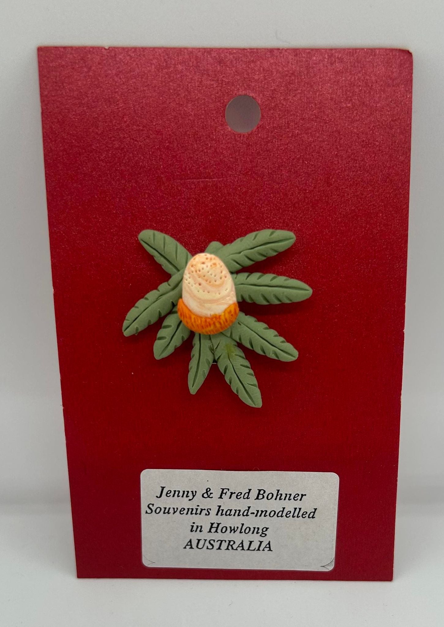 a clay badge of an orange banksia with green leaves
