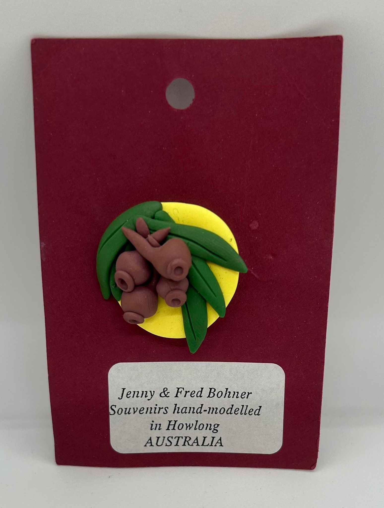 a clay badge of brown gum nuts with green leaves