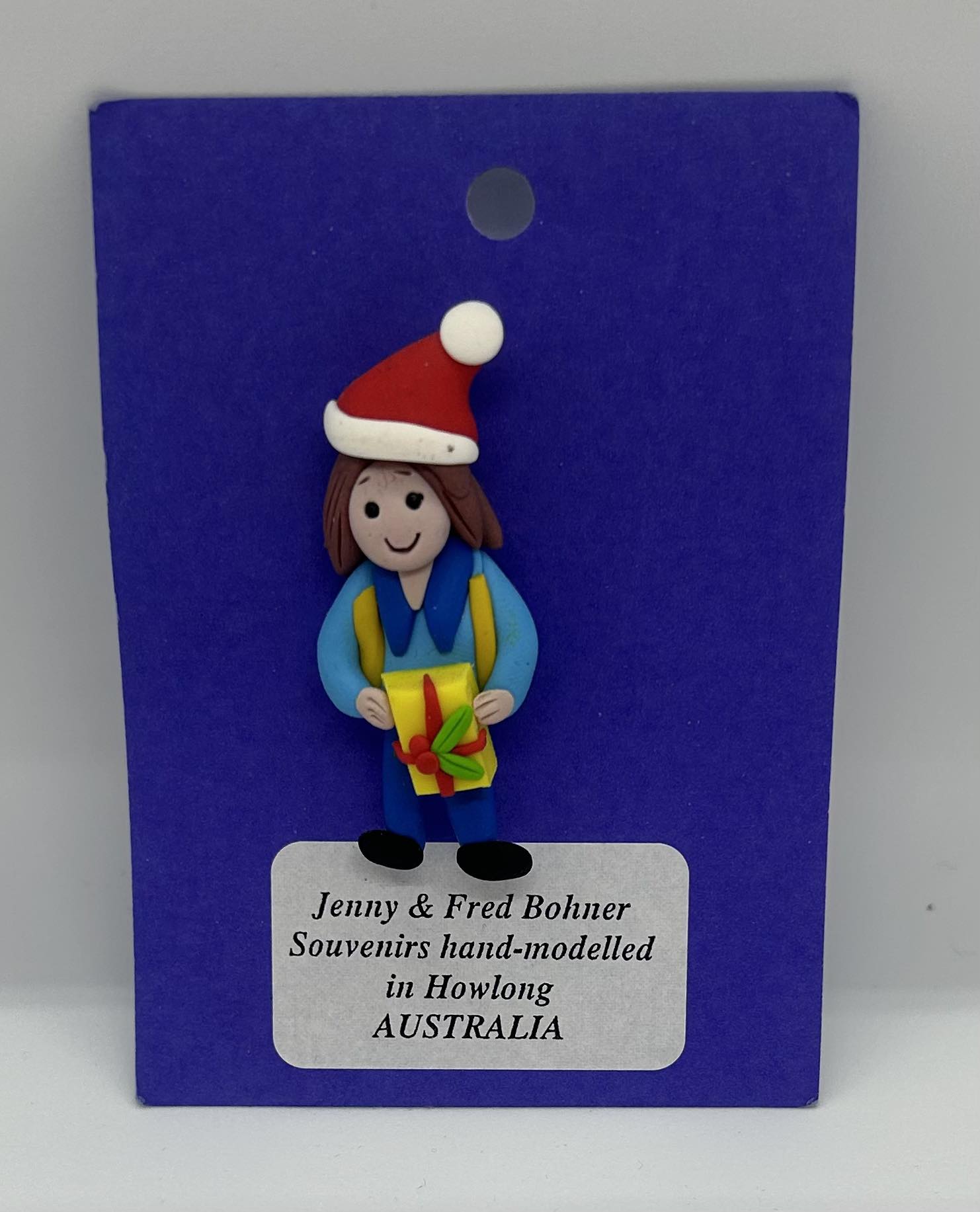 a clay badge of a leader holding a present with a Santa hat on
