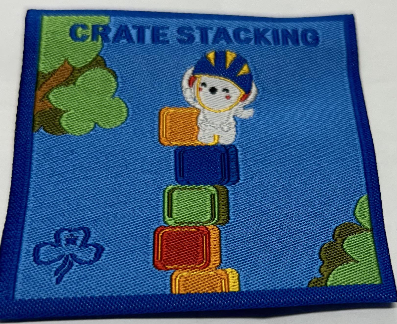 a square unbound blue badge with a koala wearing a helmet on top of some coloured crates