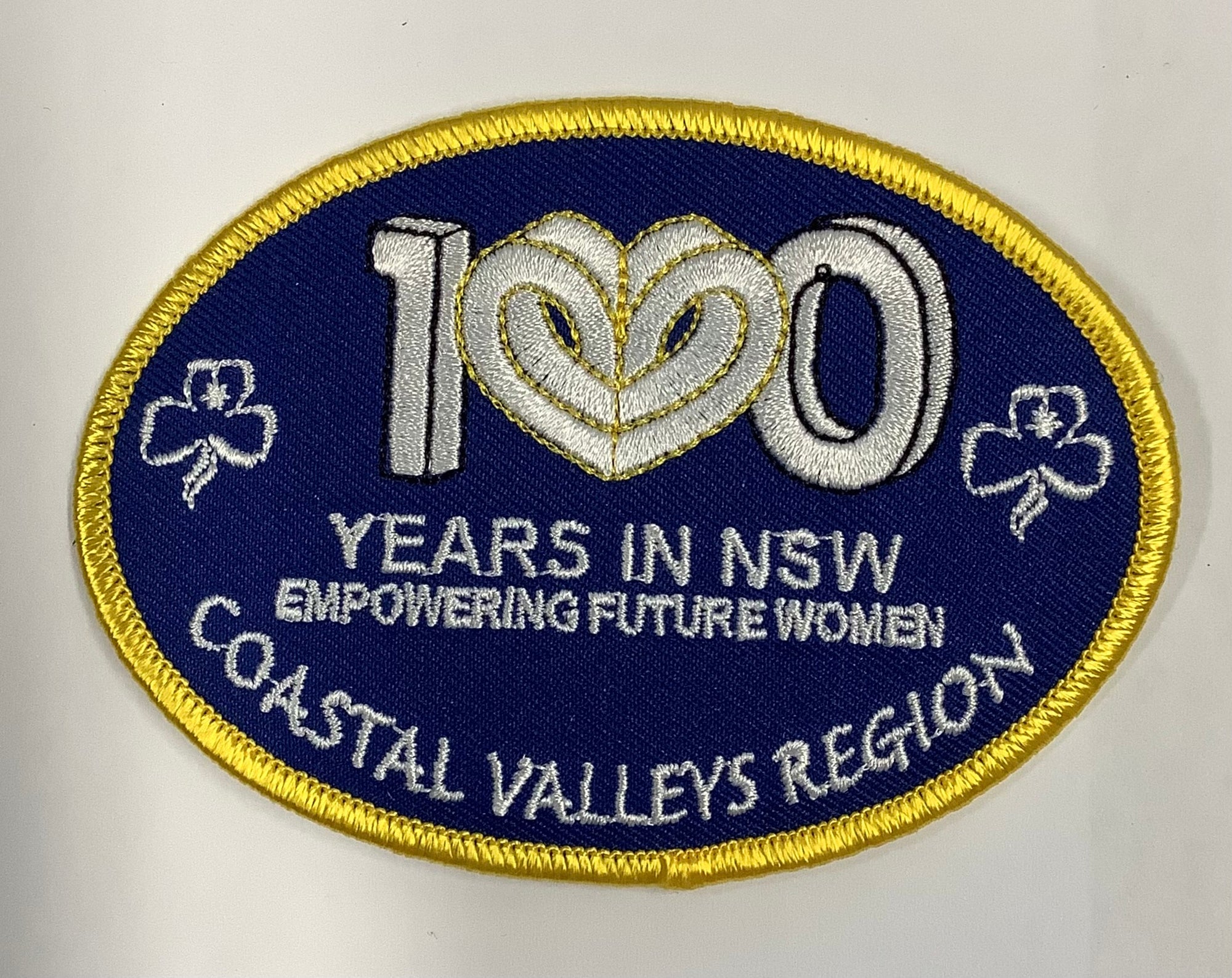 a dark blue oval shaped badge bound in gold with 100 years in NSW empowering future women embroidered on the badge