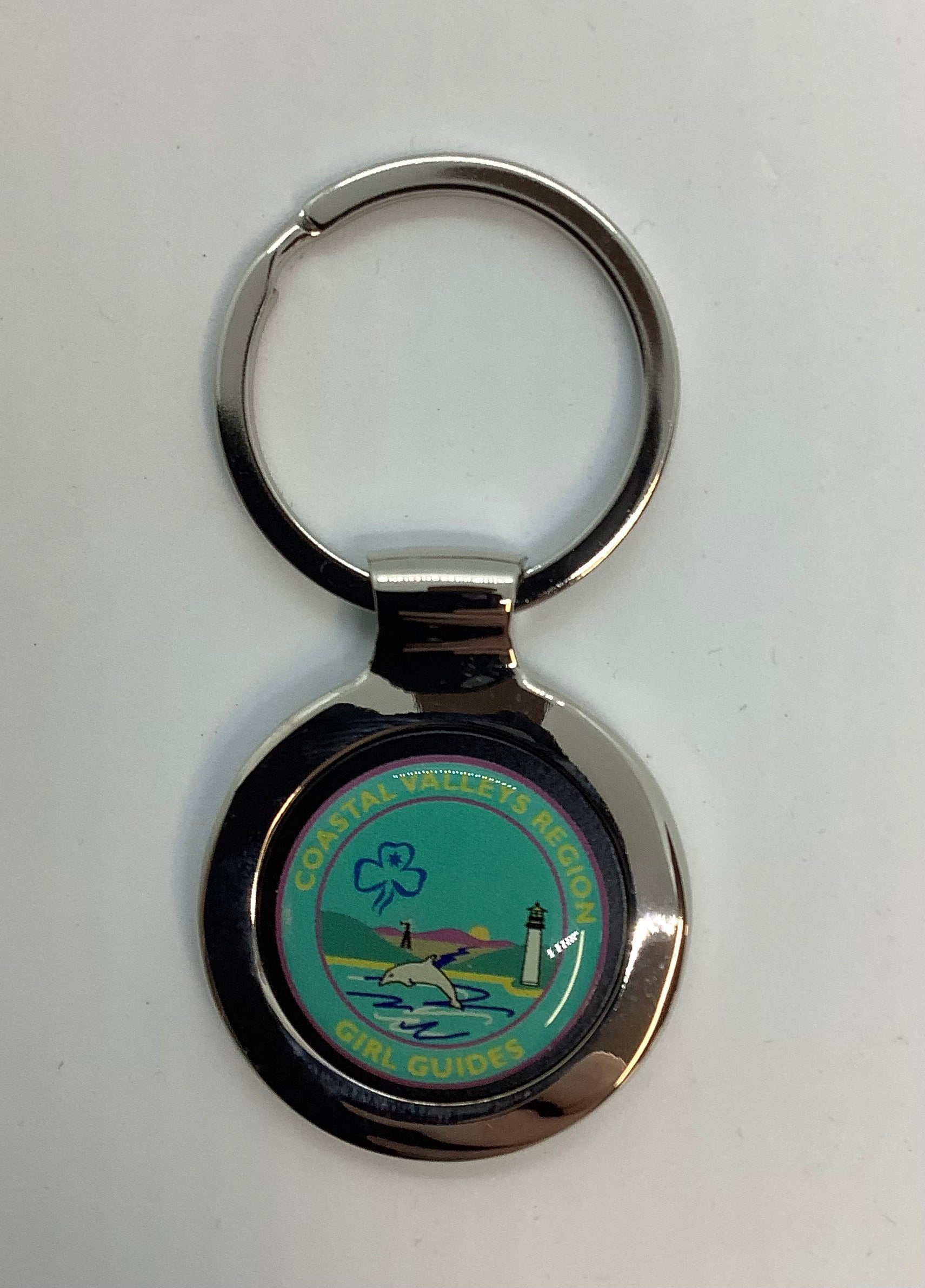a round silver key ring with CVR girl guides in gold on teal enamel with a dolphin and lighthouse 