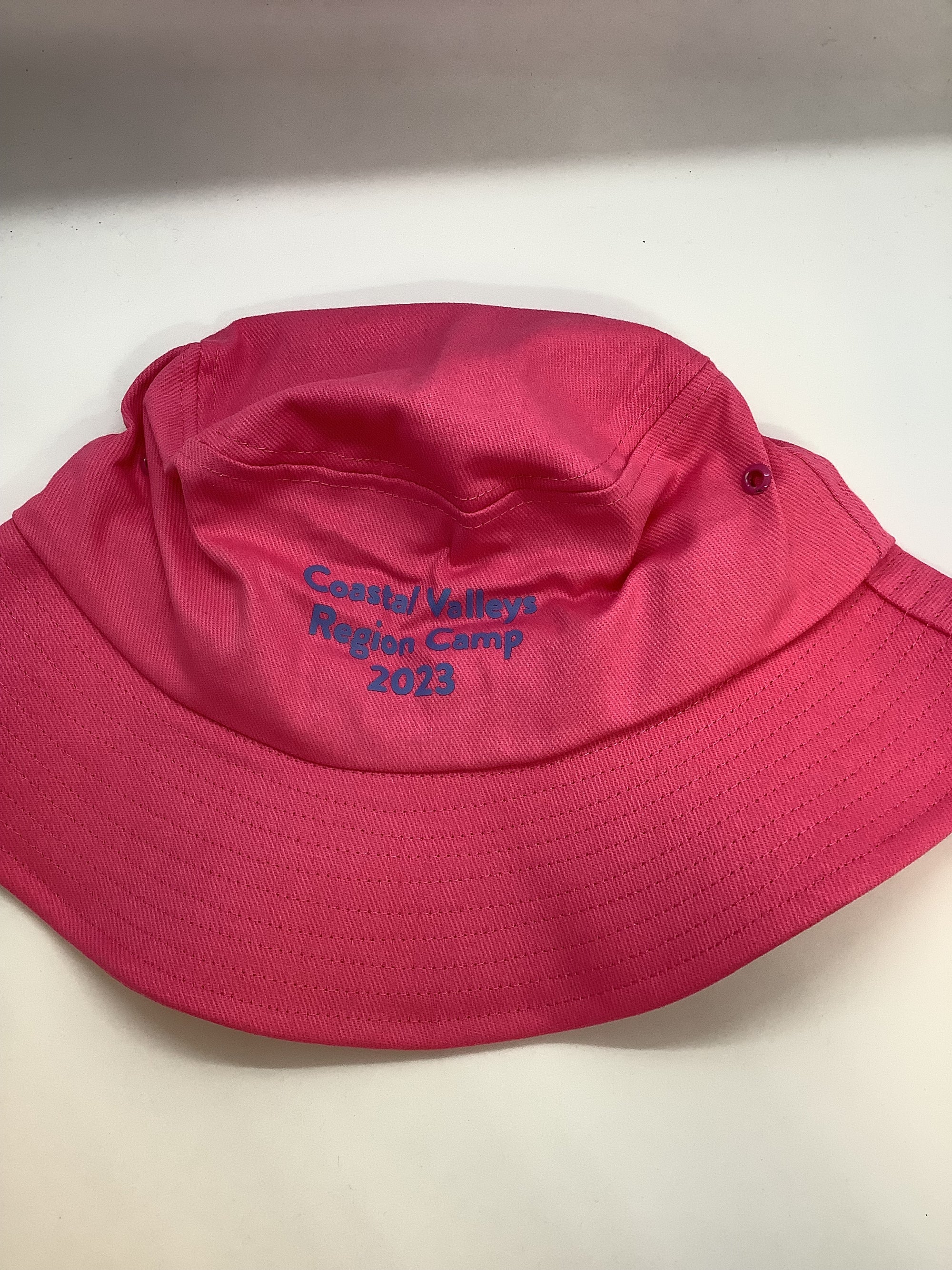 a pink bucket hat with coastal valleys region camp 2023 printed on it