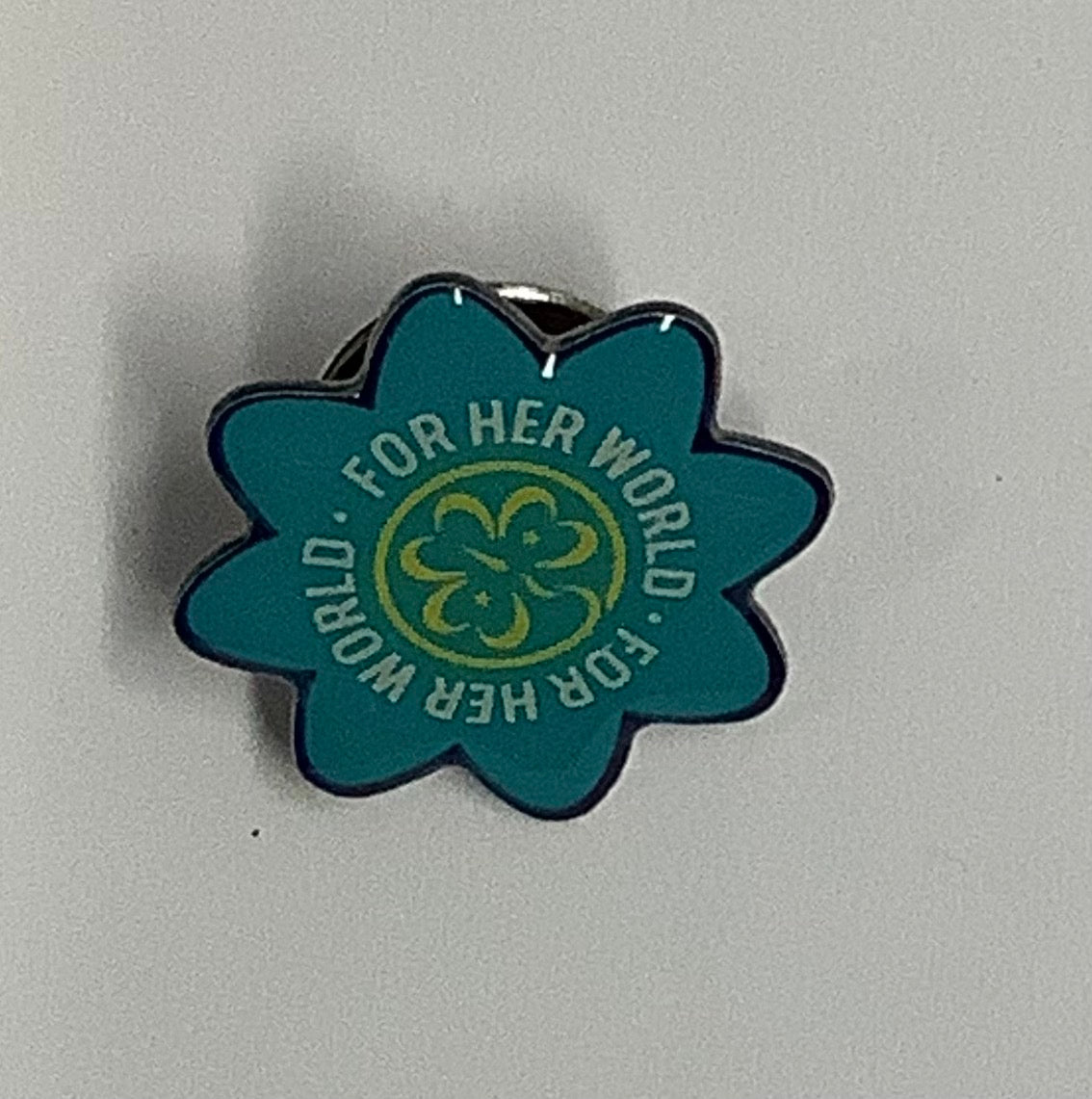 a teal metal pin in the shape of a flower with the trefoil in the centre