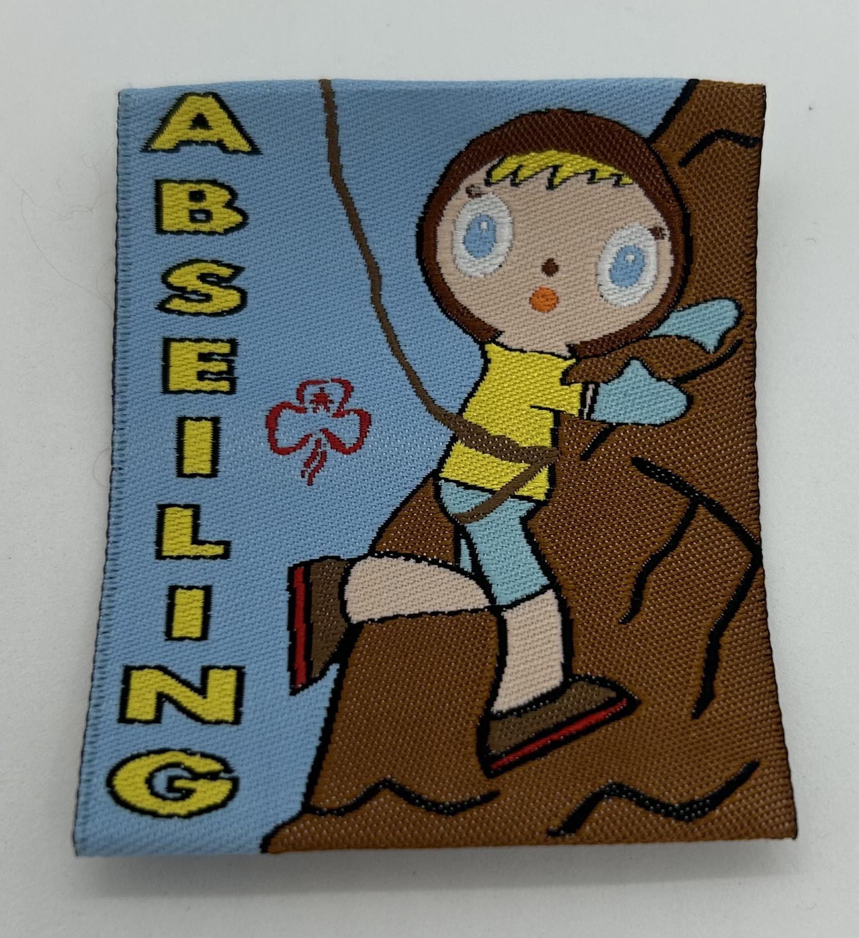 an unbound woven badge with the word abseiling in yellow and a girl on a rock face