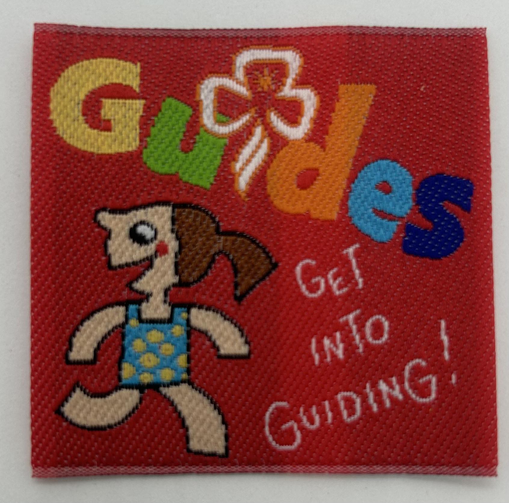 a red square unbound fun badge with a girl and the words guides get into guiding