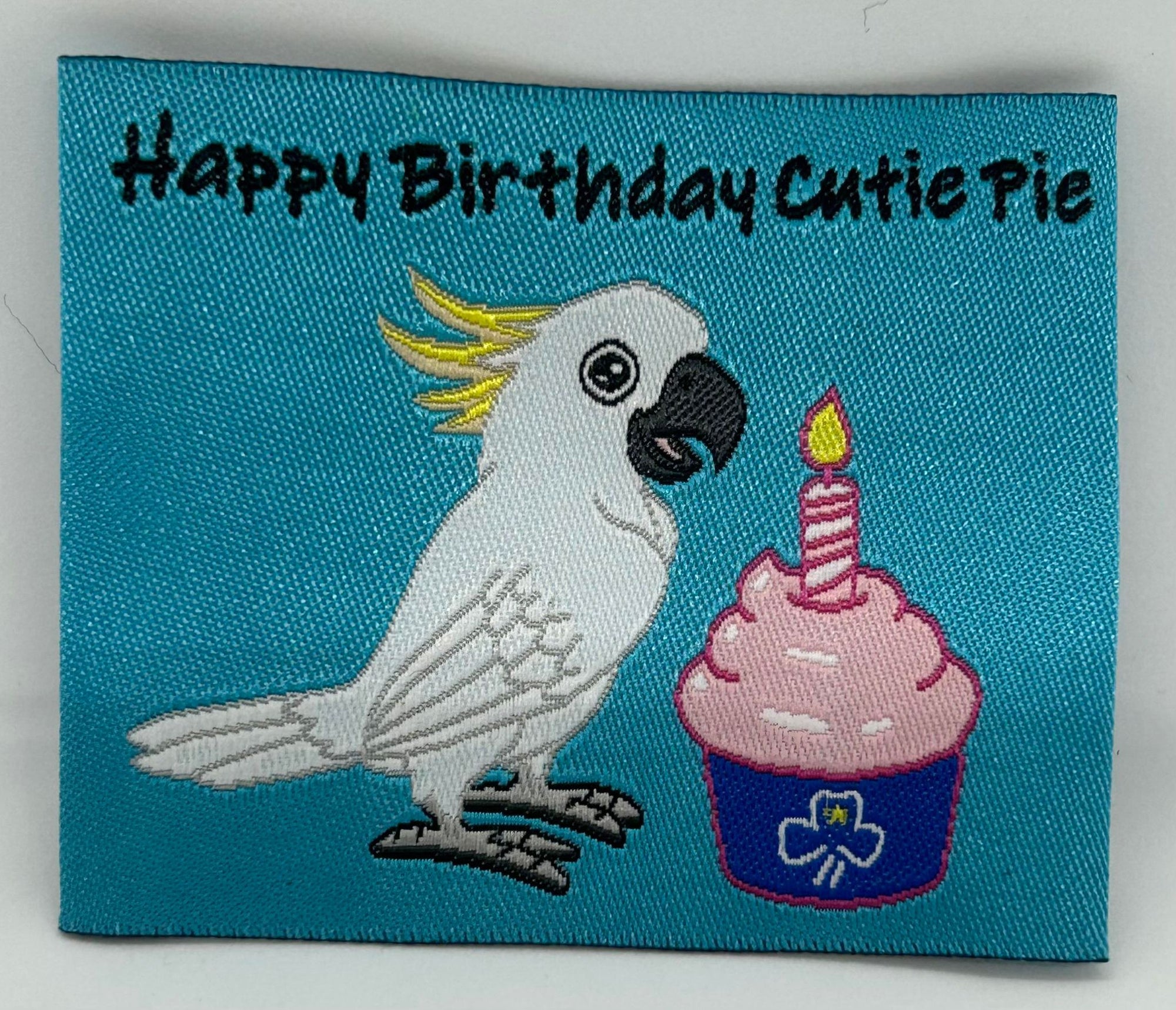 a square unbound blue badge with a cockatoo and a cup cake