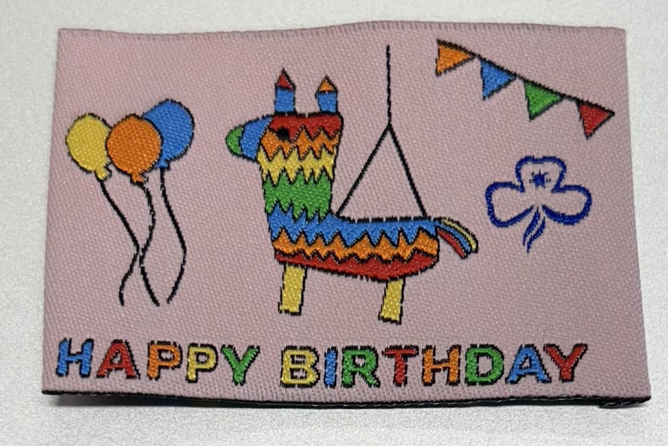 an unbound rectangular badge with a pink background with a piñata and balloons and the words happy birthday in rainbow colours