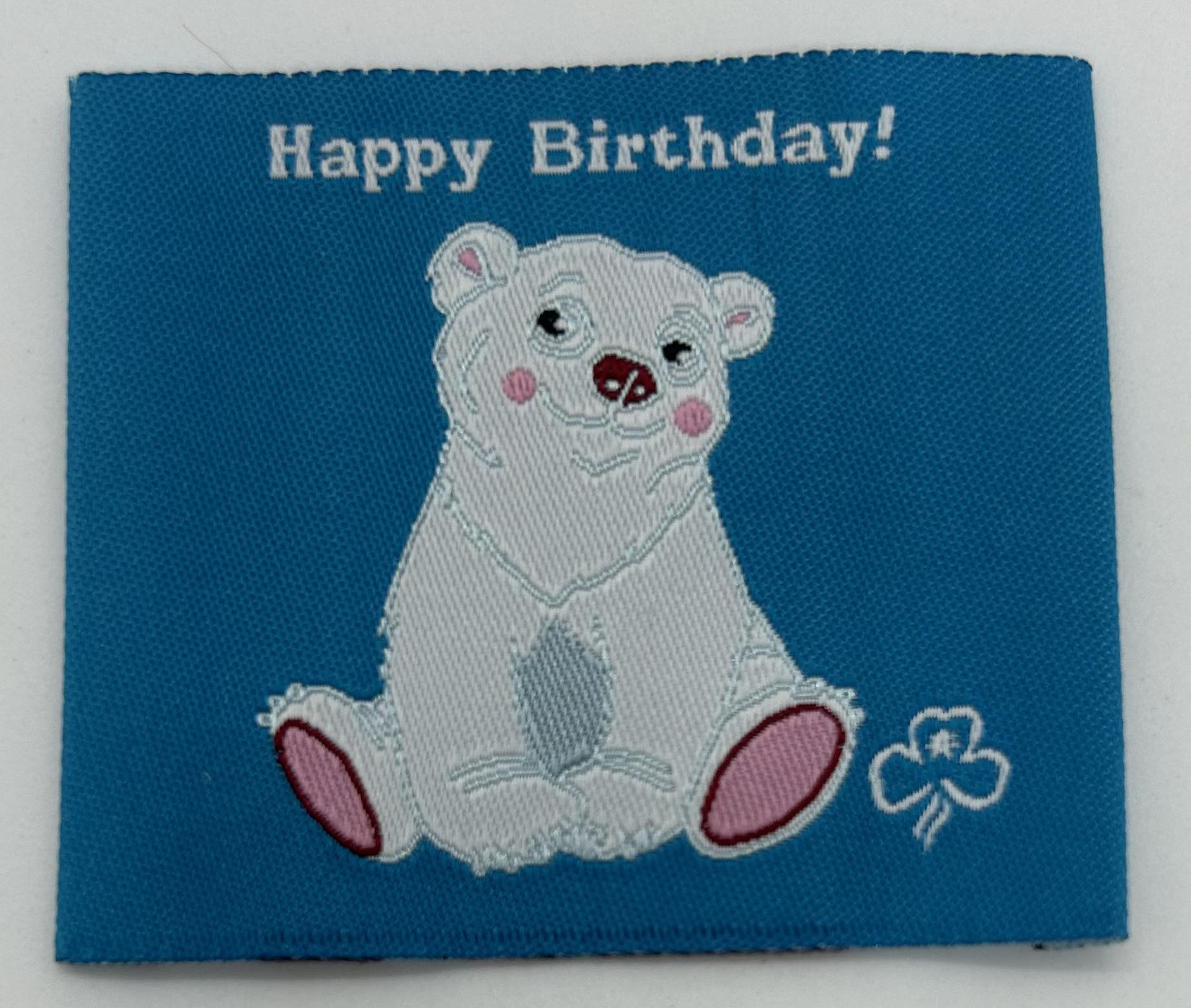 a square blue unbound woven badge with happy birthday and a white polar bear