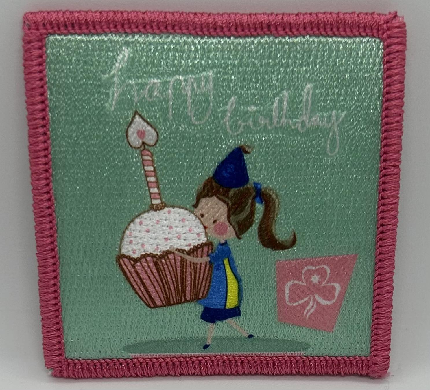a square light green badge bound in pink with a guide with a cupcake