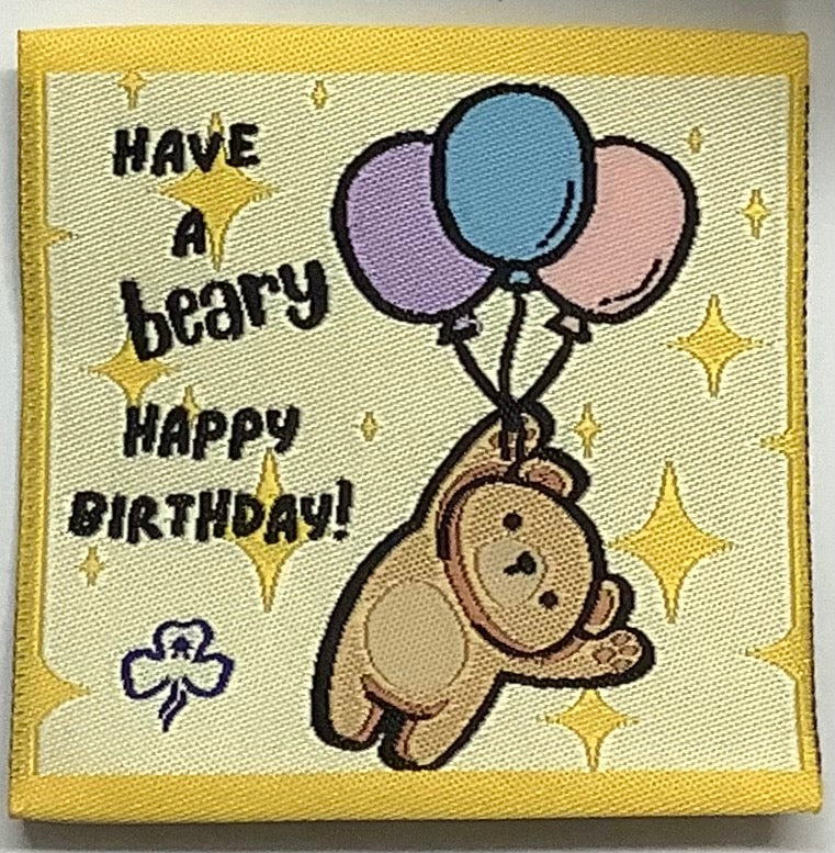 a square unbound badge that is yellow with a bear holding three balloons