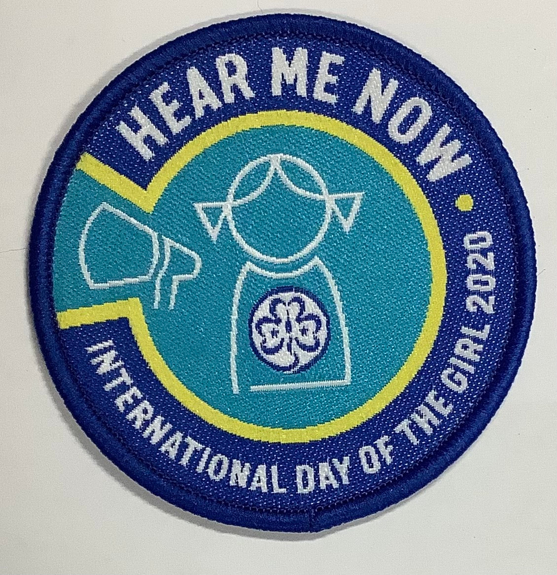 a round badge bound in blue that has a silhouette of a girl and a megaphone on it