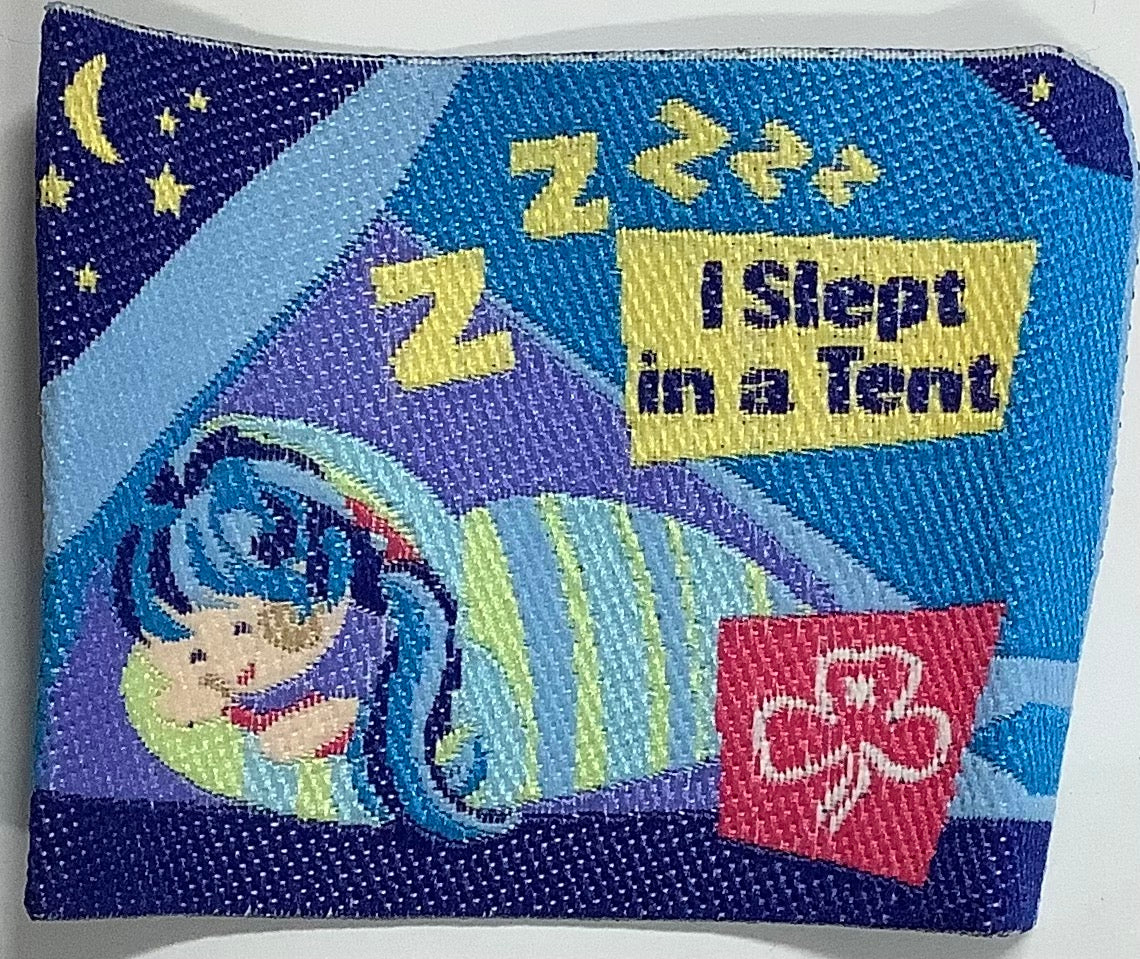 a square unbound badge that has a girl in a sleeping bag in a tent