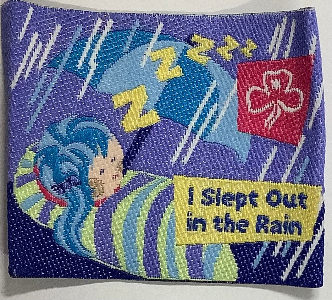 a square unbound badge with a girl in a sleeping bag in the rain with an umbrella
