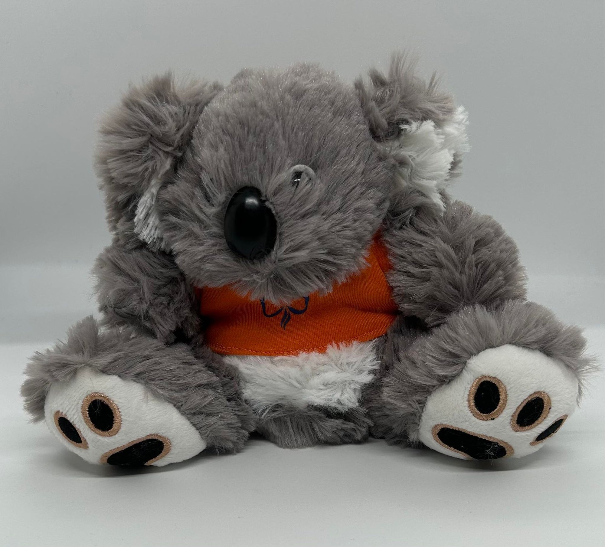 a small grey koala stuffed toy with an orange t-shirt on with a blue trefoil