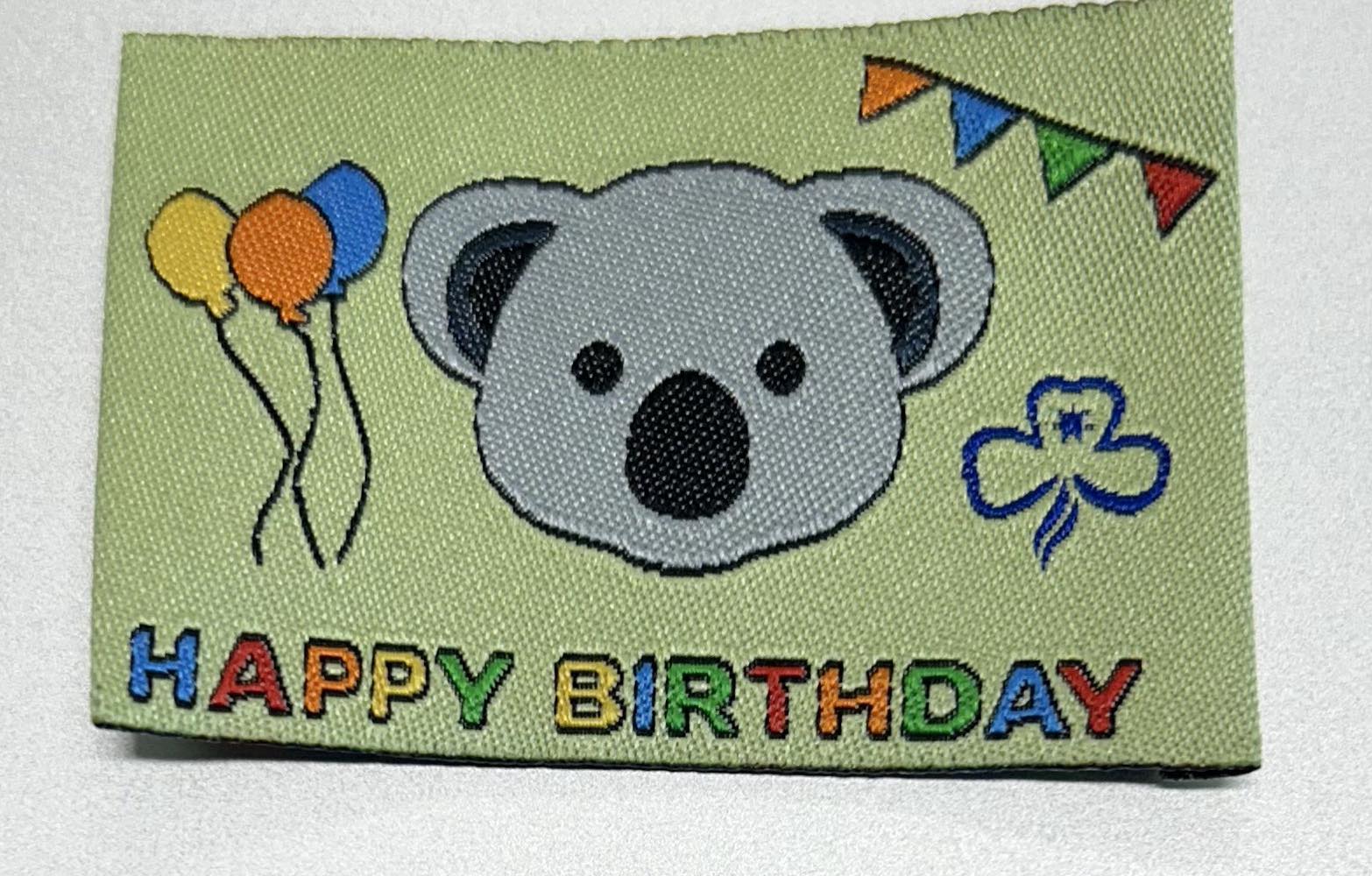 an unbound rectangular badge with a koala face with balloons and bunting in rainbow colours