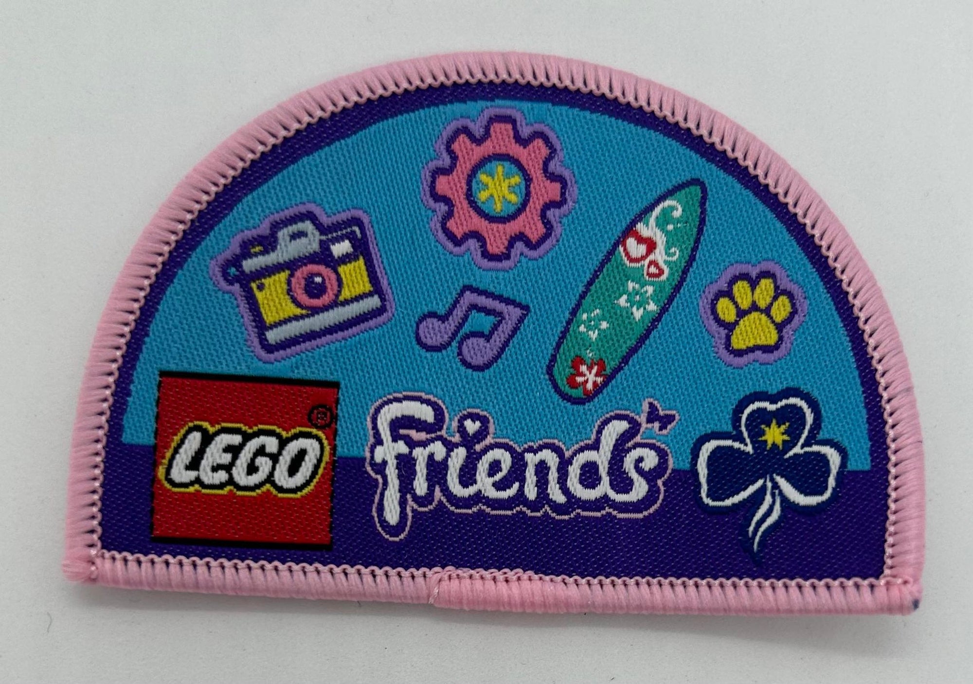 a semi circle shaped badge bound in pink with things from the lego challenge on it
