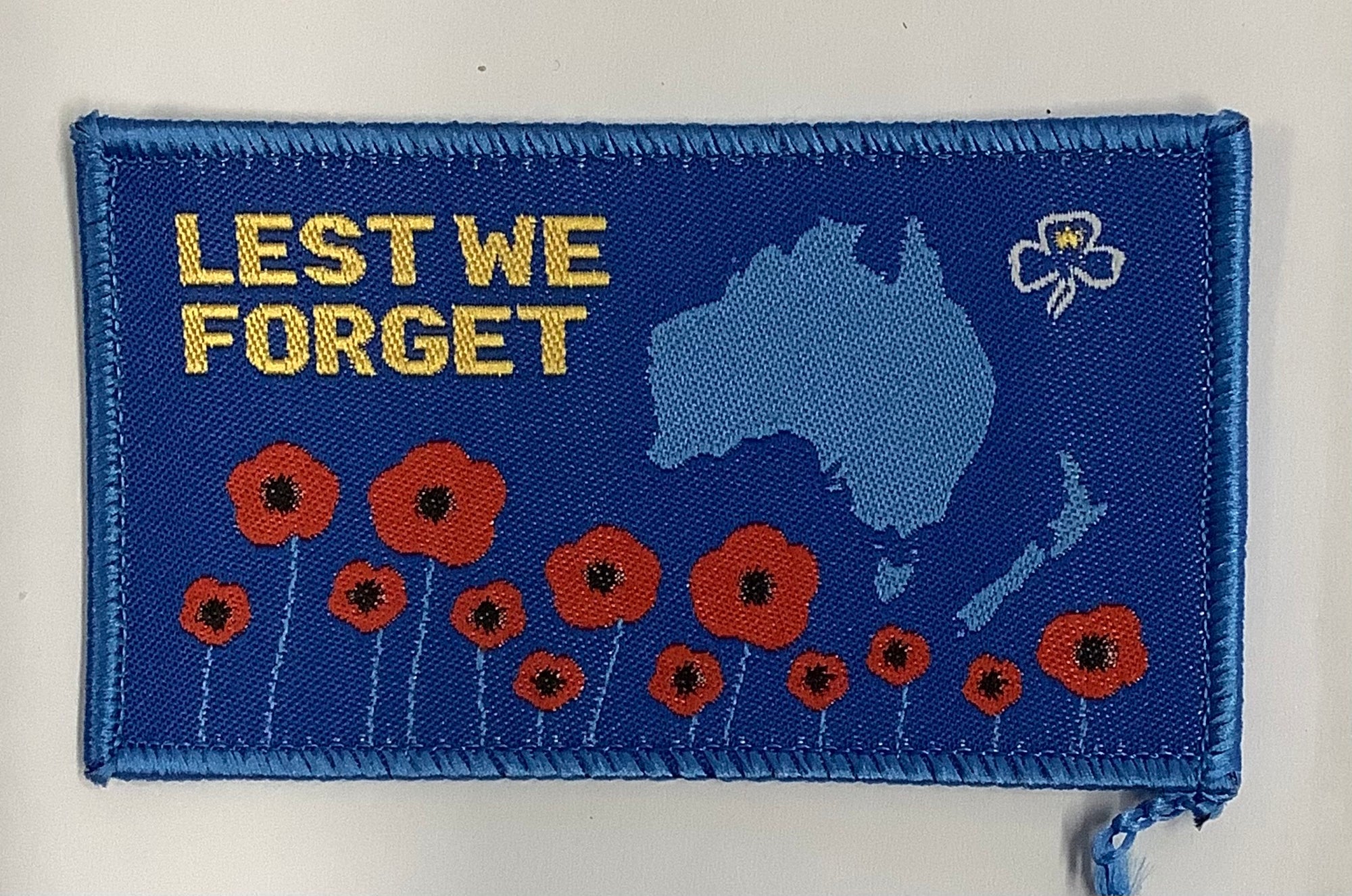 a rectangle badge bound in blue with maps of Australia and New Zealand and poppies