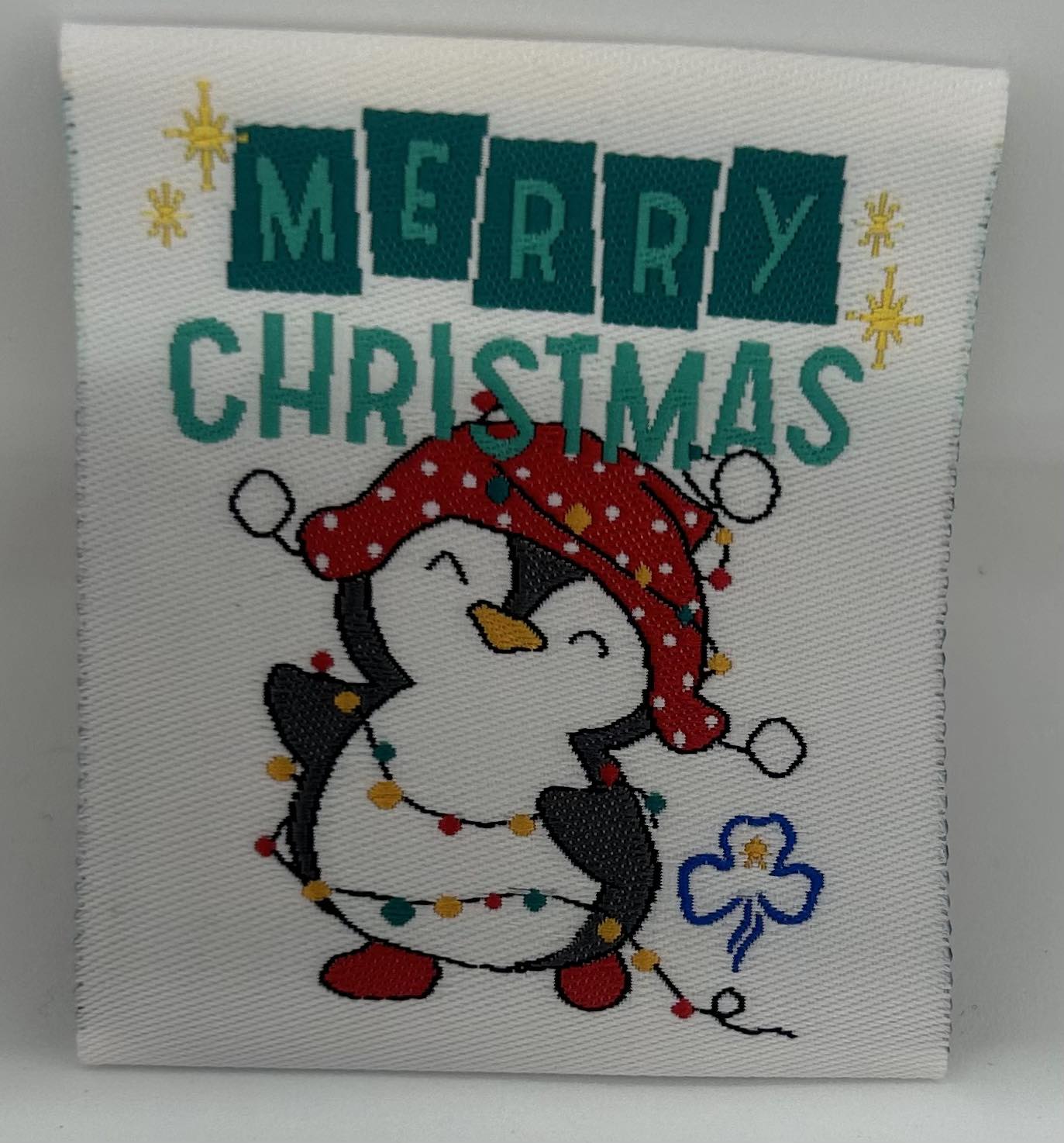 a square white unbound badge with merry Christmas and a penguin with a string of lights