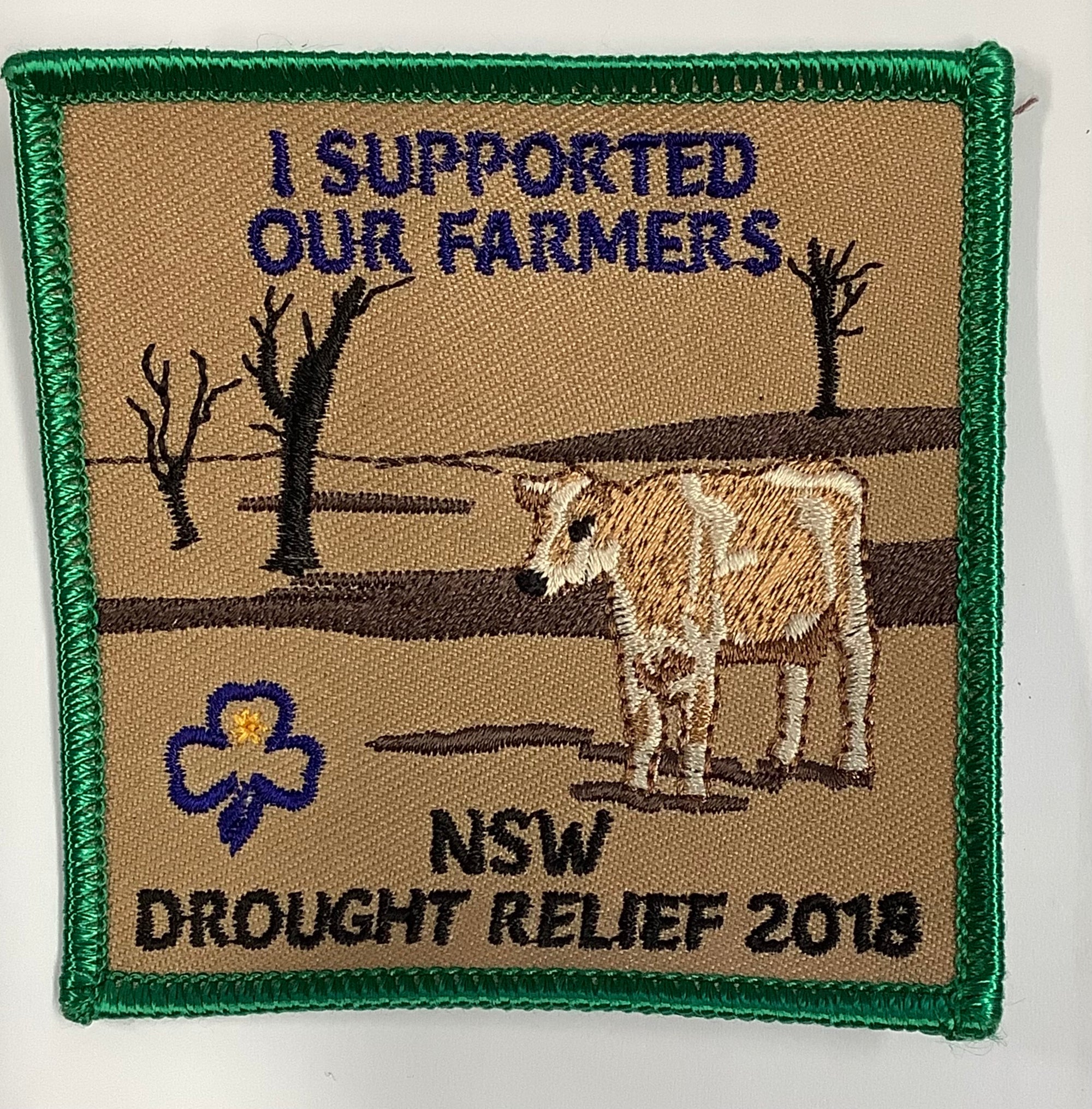a square badge bound in green with a picture of a cow and dry land