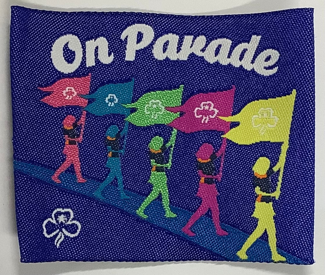 a square unbound badge in dark blue with five guides carrying flags
