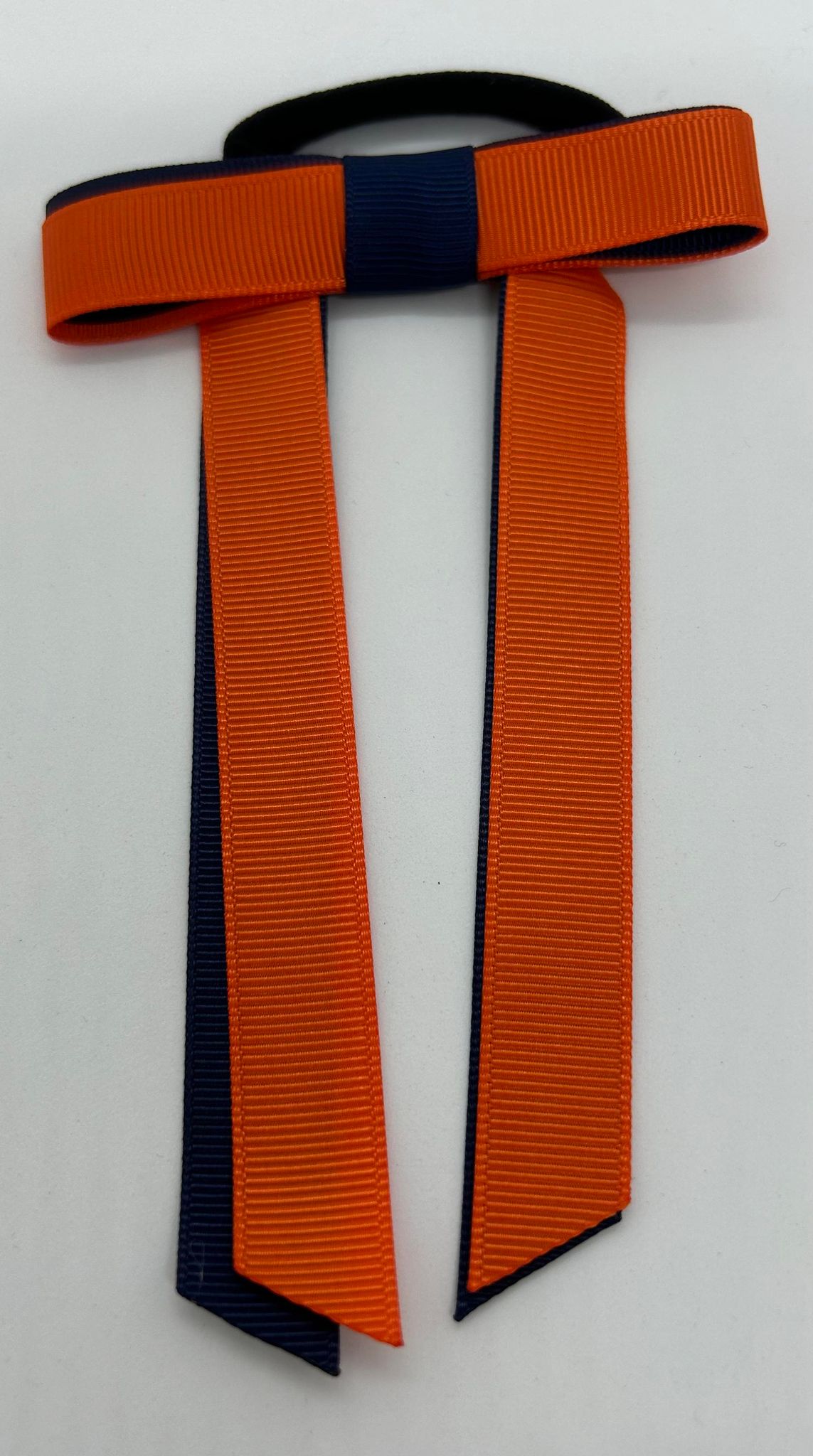 a hair bow on an elastic band with long tails in the orange and blue guide colours