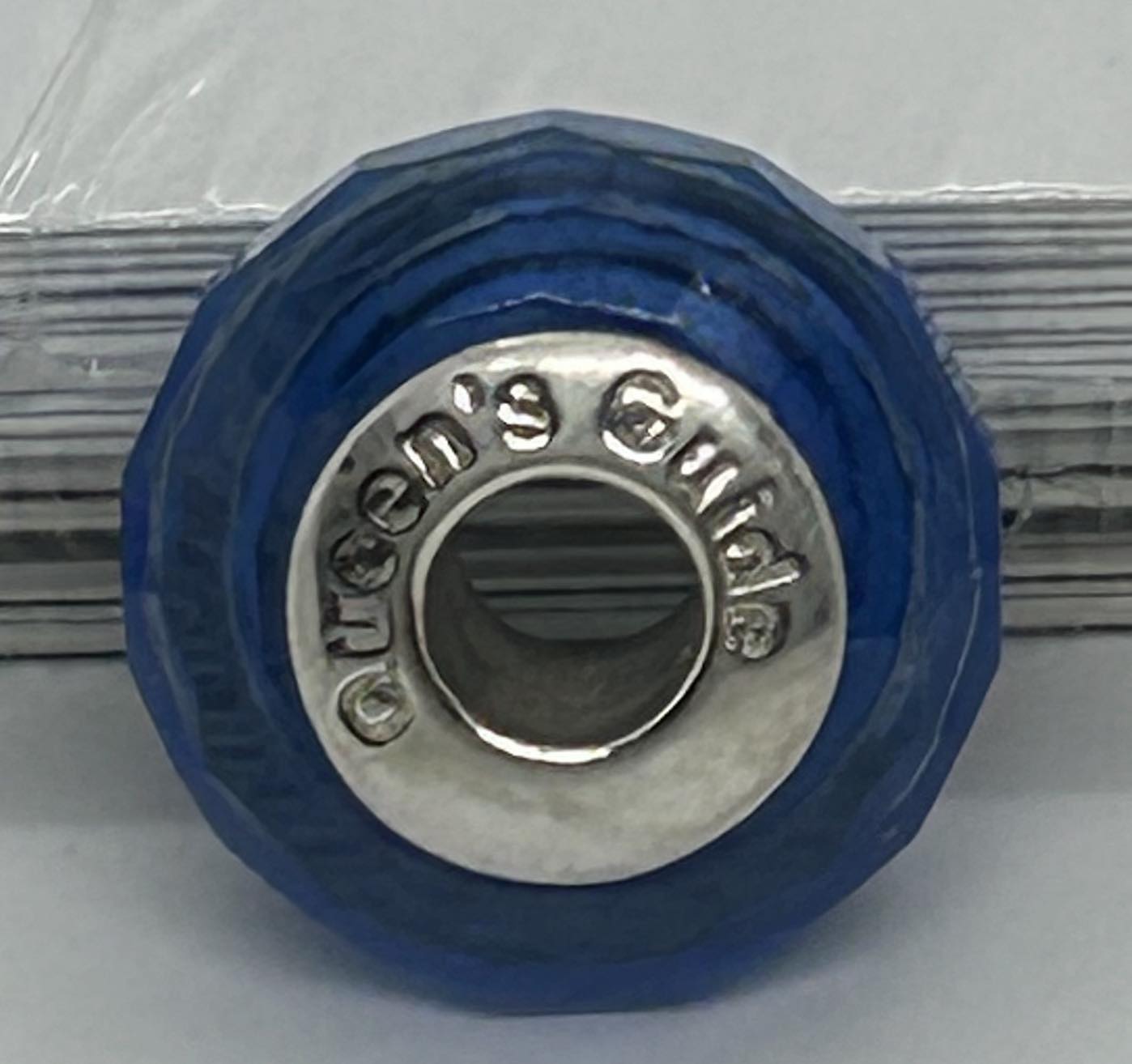 a blue pandora like charm with queen's guide stamped on the metal centre